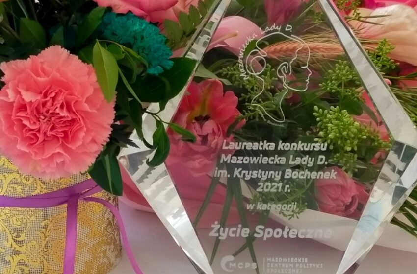 Statuetka szlkana z napisem Laureatka konkursu Mazowiecka Lady D Krystyny Bochanek 2021 w kategorii Życie Społeczke oraz kolorowe kwiaty