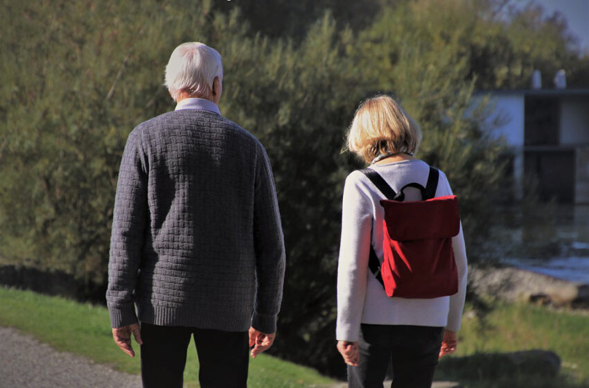 Kobieta z czerwonym plecakiem na plecach spacerująca w parku ze starszym mężczyzną