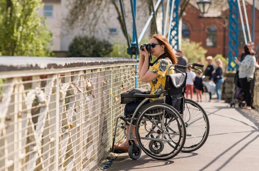 Stojąca na wózku inwalidzkim na moście kobieta, robiąca zdjęcia