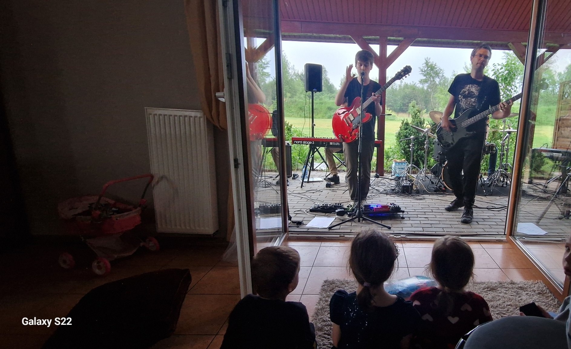 sala, na której siedzą dzieci, przed nimi scena i dwóch muzyków z gitarami